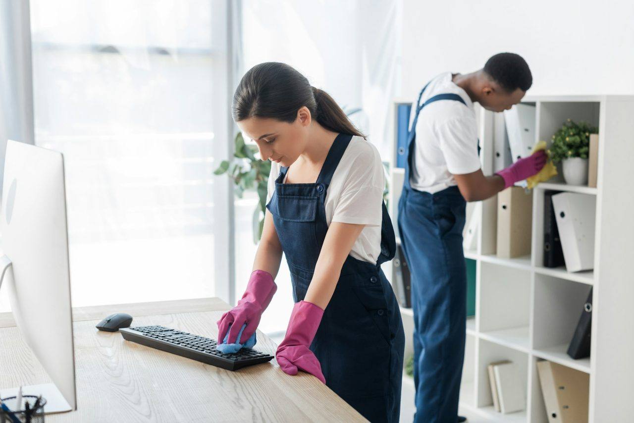 Cleaner wiping a computer keyboard at an office desk