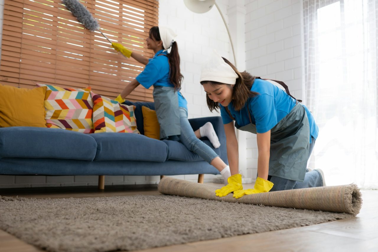 young women cleaning maid in uniform and rubber gloves are cleaning the room fold up carpet